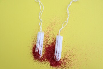 Two white tampons on yellow background with red glitter. Period concept