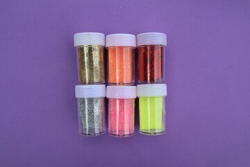 Pots of colorful glitter on purple background