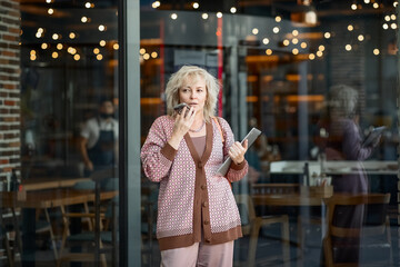 Attractive adult blonde of European appearance in a pantsuit on the streets of the city with a laptop in her hands sends a voice message on a mobile phone