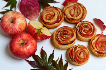 Rose shaped apple cupcakes, red apples, autumn leaves on white background. Top view photo of sweet apple pies with cinnamon and honey. 