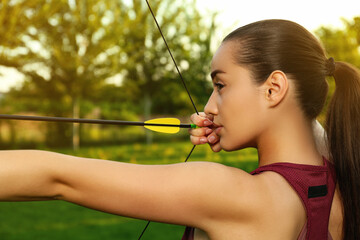Woman with bow and arrow practicing archery in park