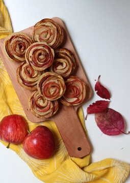 Small apple pies on wooden cutting board. Rose shaped apple cupcakes top view photo. Autumn sweets on a table. 
