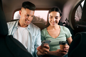 Happy couple with smartphone and cup of drink in modern taxi