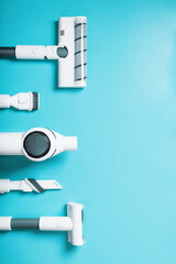 A set of nozzles and a white cordless vacuum cleaner in a row on a blue background, free space. Top view