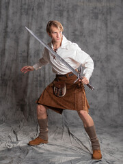 Fototapeta na wymiar A young man in a leather kilt and a white lace-up blouse. A Scottish knight