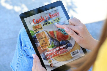 Woman reading online magazine on tablet outdoors, closeup