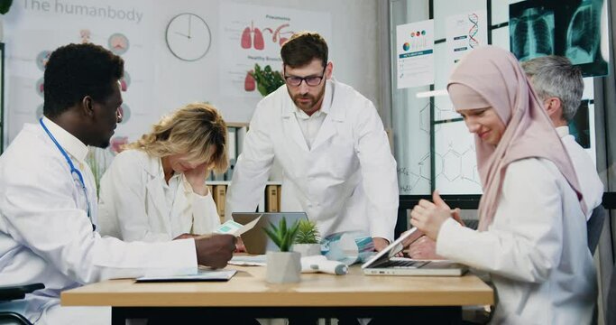 Problems in work where furious strict bearded main doctor quarreling his frightened silent multicultural workmates for bad results in joint work during meeting