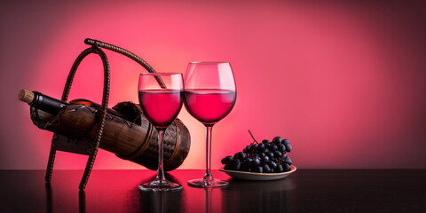  Red wine into two glasses and grape in plate on dark wooden table. Banner.