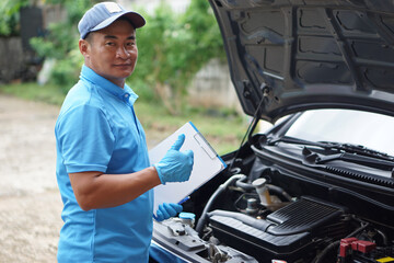 Fototapeta na wymiar Asian male mechanic raises thumb up , hold paper clipboard and stands in front of the car. Concept : Car engine checking inspection service. Car maintenance. 