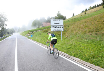 cyclist with protective helmet pedaling on the uphill road to Monte Zoncolan in Italy with rain...