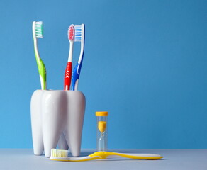 Toothbrushes are in a glass, there is an hourglass next to it, to count the time of brushing your teeth, and one brush lies on the table