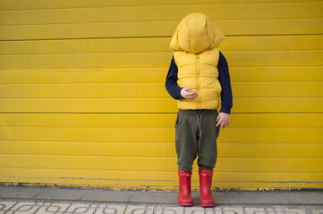 Little boy hides his face with his coat hood