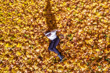 Top view. Beautiful happy young woman lying and relaxing on the autumn maple leaves in the park. Aerial, drone view