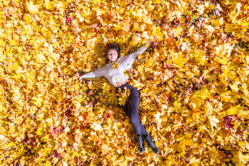 Top view. Beautiful happy young woman lying and relaxing on the autumn maple leaves in the park....