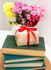 a gift on a stack with books on the background of a bouquet of flowers