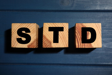 Wooden cubes with letters STD (sexually transmitted diseases) on blue table, flat lay
