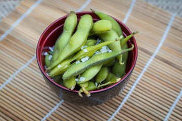 A bowl of steamed edamame beans with sea salt in a black bowl