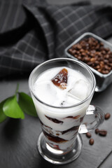 Glass cup of milk with delicious grass jelly and coffee beans on black table, closeup