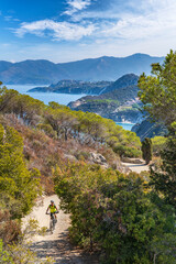 Fototapeta na wymiar nice woman riding her electric mountain bike on the coastline above the mediterranean sea on the Island of Elba in the tuscan Archipelago, Tuscany, Italy