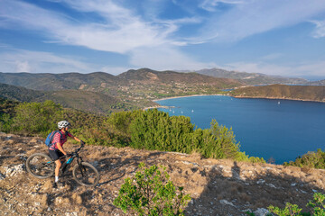 Fototapeta premium nice woman riding her electric mountain bike on the coastline above the mediterranean sea on the Island of Elba in the tuscan Archipelago, Tuscany, Italy