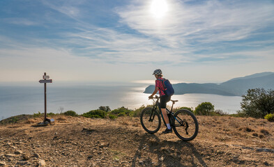 Fototapeta na wymiar nice woman riding her electric mountain bike at sunset at the coastline of mediterranean sea on the Island of Elba in the tuscan Archipelago Tuscany, Italy