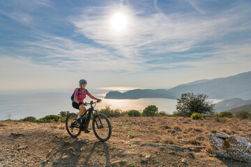 Fototapeta premium nice woman riding her electric mountain bike at sunset at the coastline of mediterranean sea on the Island of Elba in the tuscan Archipelago Tuscany, Italy