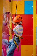 Little girl in helmet poses on climbing wall
