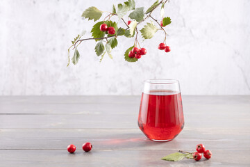  glass of hawthorn berry juice and a branch with fresh berries on a gray background