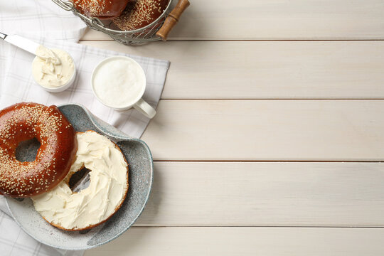 Delicious bagel with cream cheese and coffee on white wooden table, flat lay. Space for text