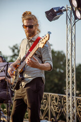 Bearded male guitarist playing guitar on outdoor stage