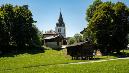 Picturesque alpine summer landscape view with small white church, wooden buildings,  trees and green pastures - Cergnat, Ormont-Dessous near Aigle in Swiss canton of Vaud, Switzerland - obrazy, fototapety, plakaty