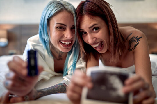 Delighted lesbian couple showing ultrasonic image of future baby