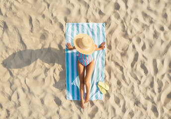Woman sunbathing on beach towel at sandy coast, aerial view
