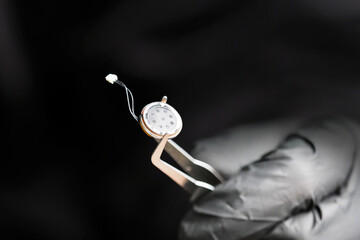 Small microphone of the overhearing device, spy holding a microphone with tweezers, black gloves. Micro listening device