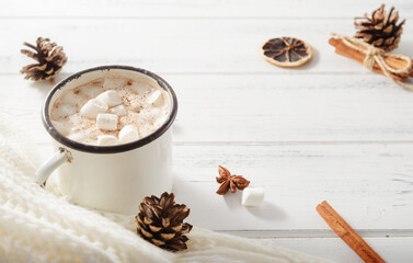 Fototapeta premium hot chocolate with marshmallows, cinnamon sticks, fir cones, white sweater on a white wooden background, top view