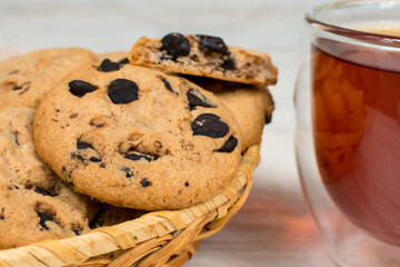Chocolate cookies in a basket close-up on the background of a glass cup of tea on a white wooden table.