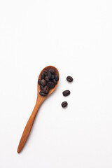 Isolated coffee beans in a wooden spoon with some beans at the side