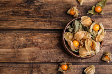 Ripe physalis fruits with dry husk on wooden table, flat lay. Space for text