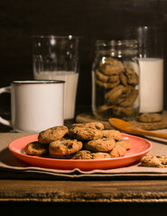 A pink plate of chocolate chip cookies, with a coffee mug, glass of milk and a jar of cookies
