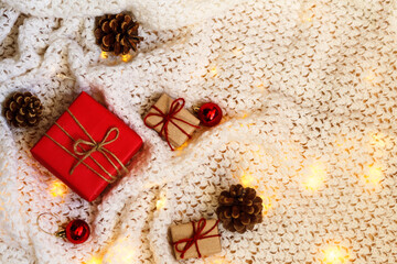 Gift boxes with pine cones and Christmas lights on a knitted white background