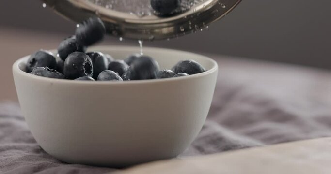 Slow motion washed ripe blueberries fall in white bowl wit copy space