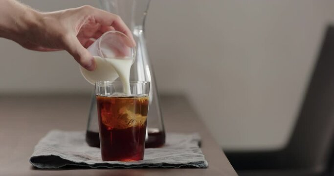 Slow motion milk pour cold in brew coffee in tumbler glass on walnut table