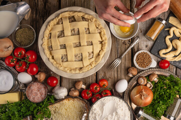 The cook prepares a pie with meat and mushrooms. The top of the cake is decorated with a dough grate. Ingredients. Lots of facilities. Wooden texture. High angle view.