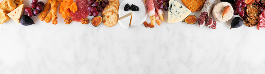 Variety of cheese and meat appetizers. Above view top border on a white marble banner background...