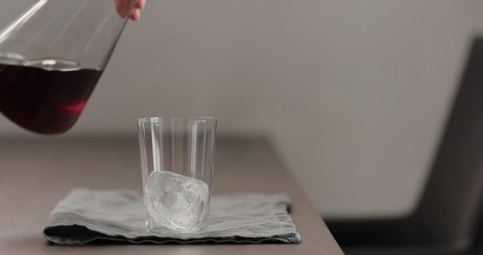Slow motion pour cold brew coffee in tumbler glass on walnut table