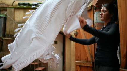 Woman shaking dust off from bedsheet cleaning home during weekend