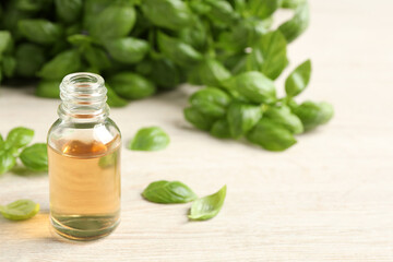 Glass bottle of basil essential oil and leaves on white wooden table. Space for text