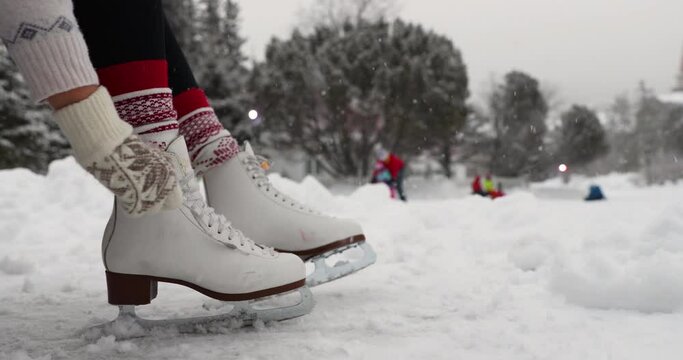 Ice skating in winter. Woman tying laces on ice skates going skating on outdoor skating rink in the snow. Idyllic snowing winter weather