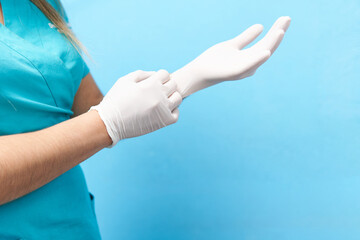 young latin dentist woman dressed in blue, detail putting on white gloves, blue background, copy...