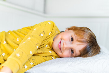 Close up portrait of a little preschool boy wering pajamas and  lying on a bed. Child smiling at...